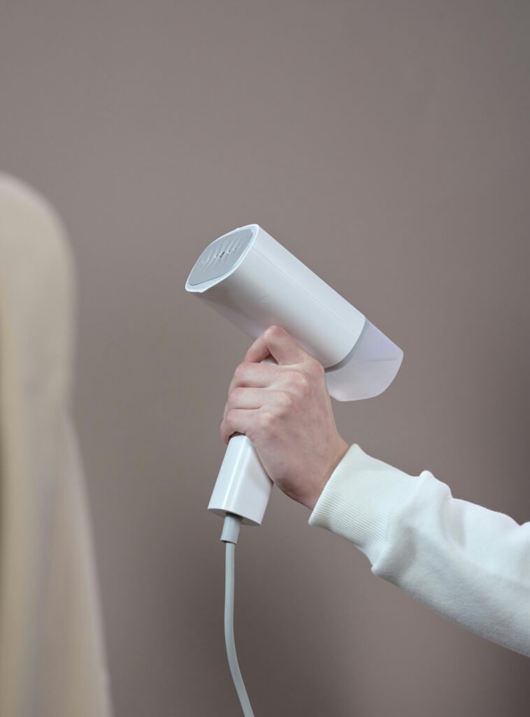 Hand holding a white hair dryer against a minimalist gray background in a studio setting.